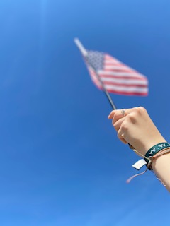 Sophomore, Gabby Burgess, holds an American flag proudly under a scenery of a blue sky.