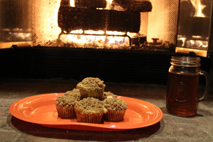 Pumpkin cream cheese filled muffins sitting in front of a stone fireplace. A glass full of apple cider is next to the delicious treats.