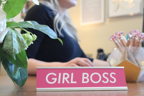 A CEO decorates her office space with a “Girlboss” desk sign. 