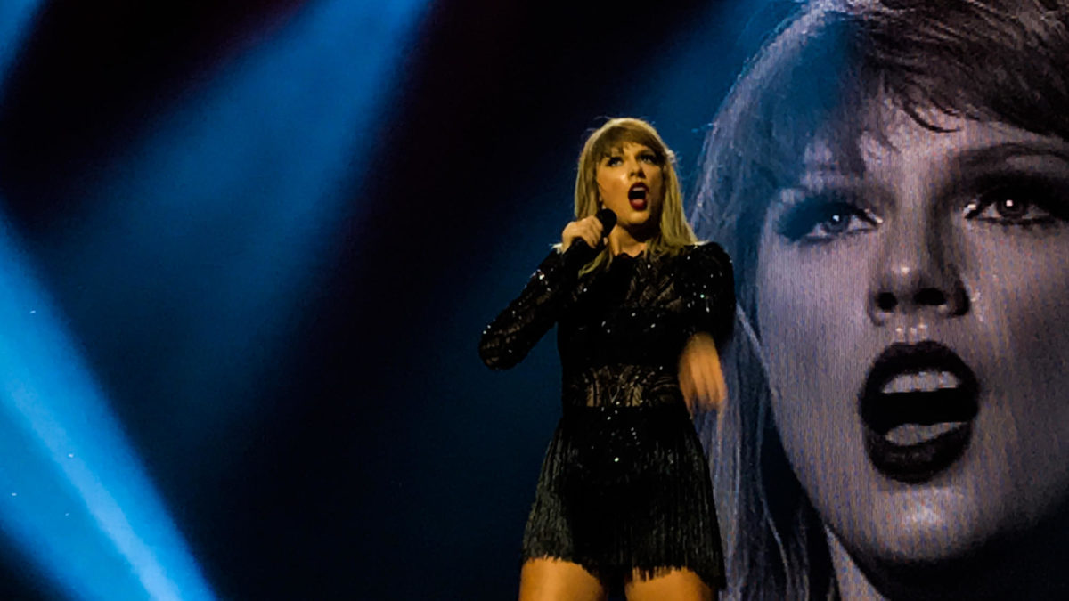 Taylor+Swift+singing+during+one+of+her+concerts+with+a+projection+of+her+face+in+the+back.+
